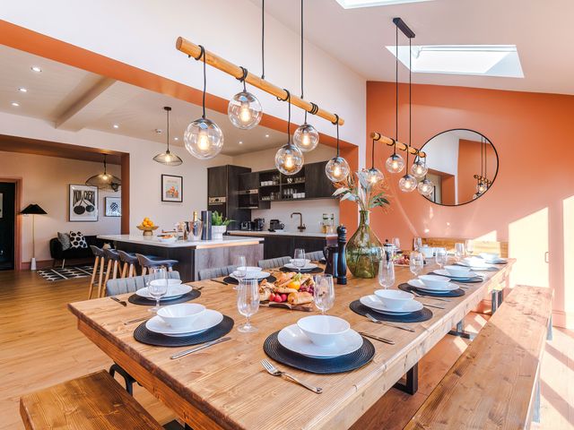 A dining area with a wooden table set for ten with plates bowls and glasses next to a kitchen with dark cabinets at Cabin Hill in Rhos-On-Sea