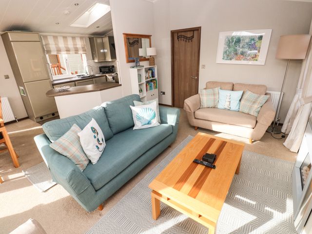A living room with a blue sofa and a beige armchair a wooden coffee table and a kitchen area at Hafan Lodge 85 Wisemans Bridge near Saundersfoot