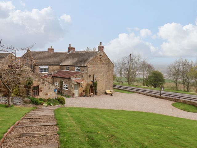 A stone house with a gravel driveway and green lawn near a road at The Cottage in Easington near Staithes