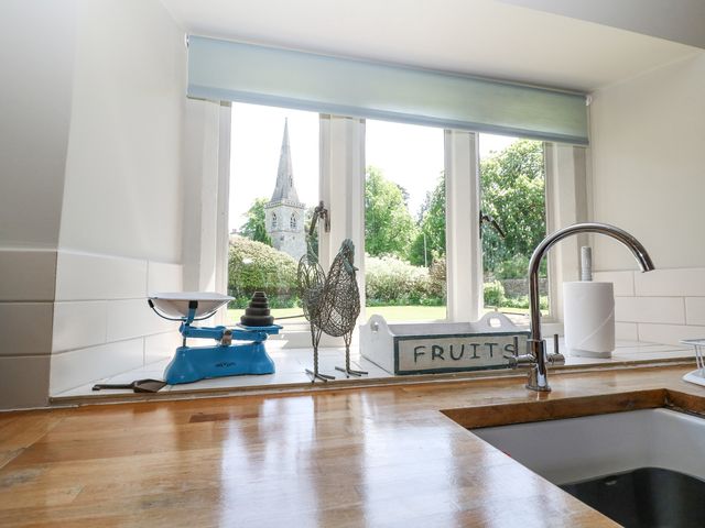 A kitchen counter with a wooden surface a chrome faucet a blue weighing scale a wire chicken decoration and a white wooden fruit crate on the windowsill at Church View Lower Slaughter
