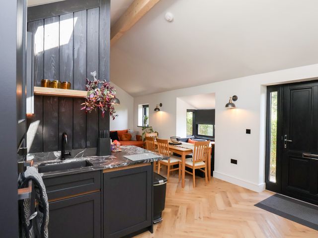 A kitchen with black cabinets and marble countertop adjacent to a dining area with wooden chairs and a black door at The Haven in Cloughton near Burniston