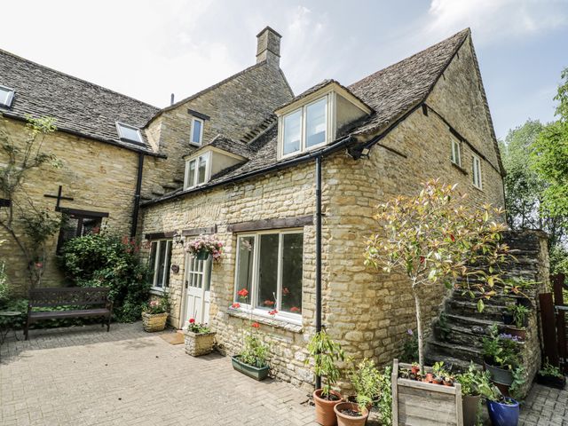 A stone building with a door and windows and a garden area at Dairy Cottage in Witney