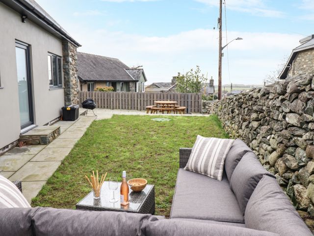 A garden with a gray outdoor sofa and table with snacks and drink near a stone wall at Bryn Hafod in Dyffryn Ardudwy