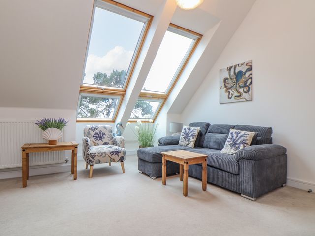 A living room with a blue sofa and patterned armchair next to wooden tables under skylight windows at Upper Deck in Truro