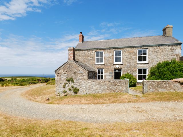 A stone farmhouse with chimneys and multiple windows near a gravel driveway and grassy area at Bosistow Farmhouse in St Levan near Porthgwarra
