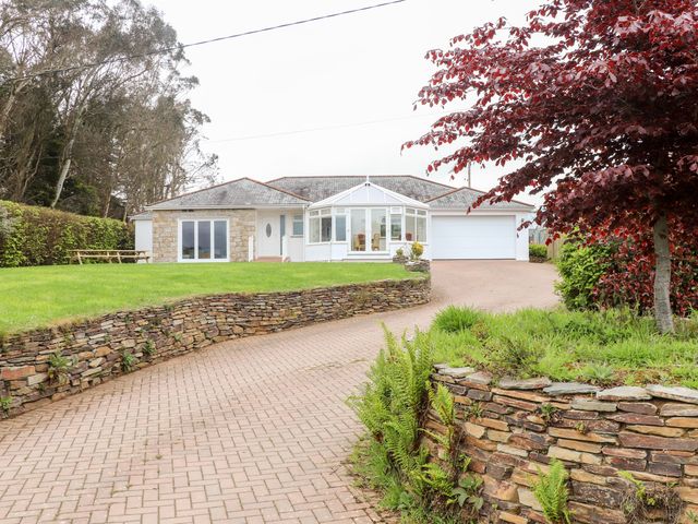 A driveway leading to a bungalow with a conservatory and attached garage surrounded by grass and trees at Took Some Doing in St Tudy