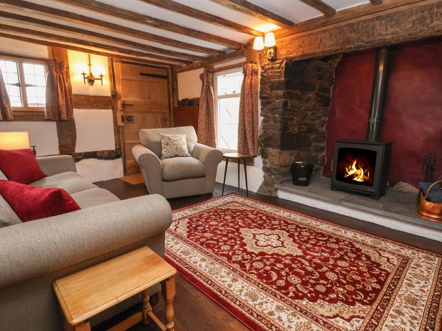 A living room with a sofa and armchair near a wood burning stove on a patterned rug at 18 Church Street in Llangollen