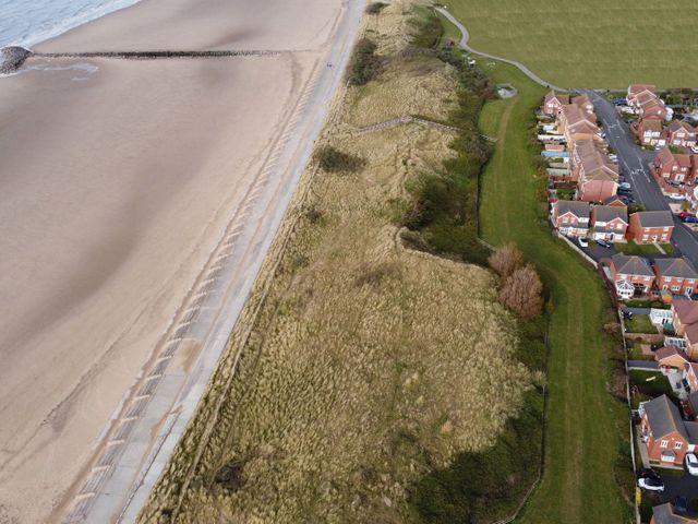 A beach with a concrete walkway beside grassy dunes and a residential neighborhood at Beachside in Prestatyn