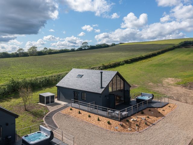 A detached black house with a deck and hot tubs surrounded by gravel and fields at Eagles Peak in Allerton near Thornton-Le-Dale