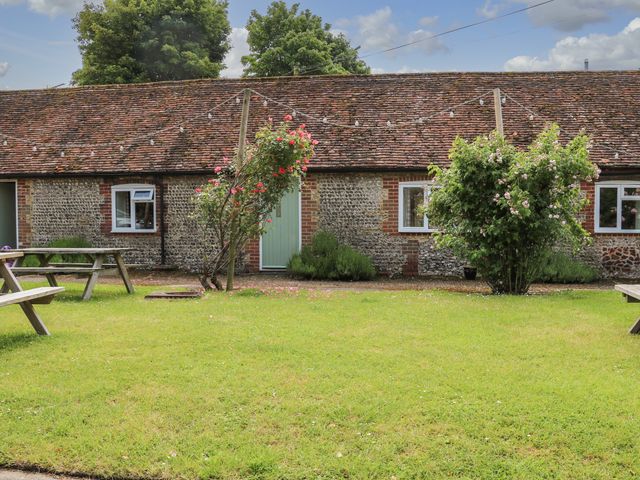 A grass lawn with two wooden picnic tables flowers on bushes and a row of stone cottages at Byre Cottage 4 in Sullington near Storrington