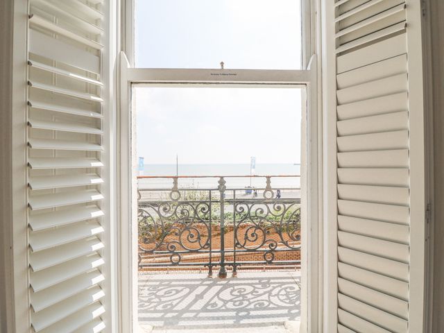 A balcony with decorative railing overlooking a beach and sea visible through a window with shutters at Sunrise Apartment in Weymouth