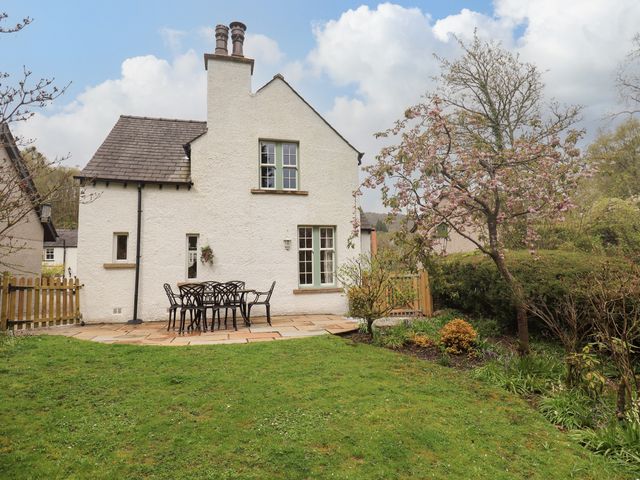 A garden with a patio table and chairs next to a white house with two chimneys and a flowering tree at The Old Post House at Low Stott Park near Newby Bridge