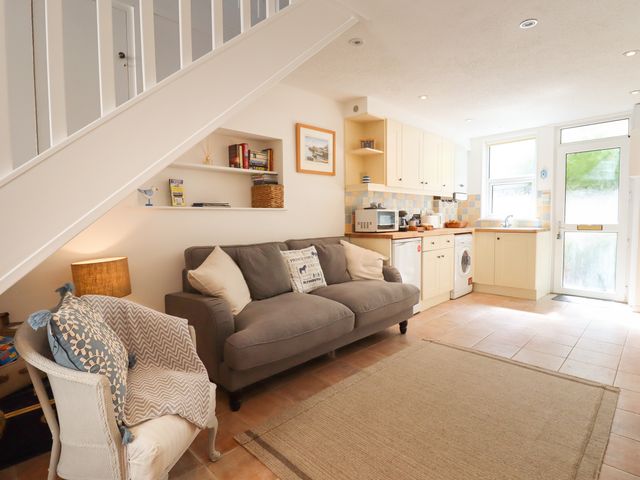 A living area with a gray sofa and white armchair next to a small kitchen at Quayside Cottage in Teignmouth
