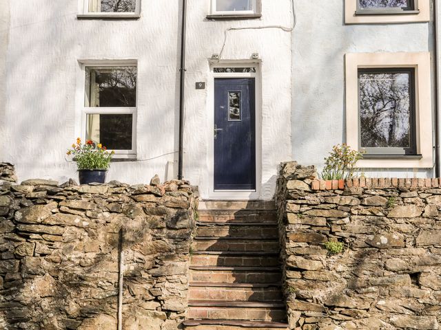 Stone steps leading to a blue front door of a white house with stone walls and windows on either side at 9 Ty Du Road Llanberis