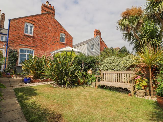 A garden with a wooden bench surrounded by plants and a brick house in the background at ODYSEA in Weymouth