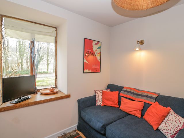 A small living area with a blue sofa and orange cushions next to a wooden window sill with a small television at The Old Stables in Usk