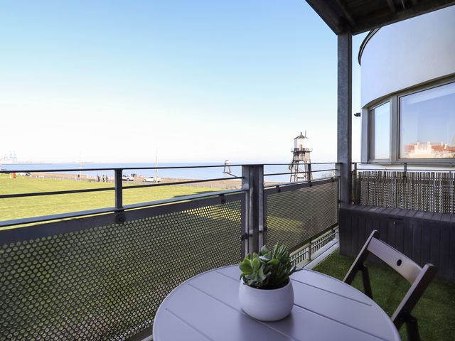 A balcony with a round table and chair overlooking green grass and the sea at Flat 19 By The Beach in Harwich
