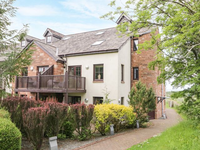 A residential building with a balcony surrounded by bushes and trees at Cosy Corner in the Lakes Greystoke