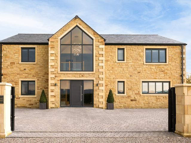 A stone house with large central glass windows and a paved driveway at Mylstone House in Langho Lancashire