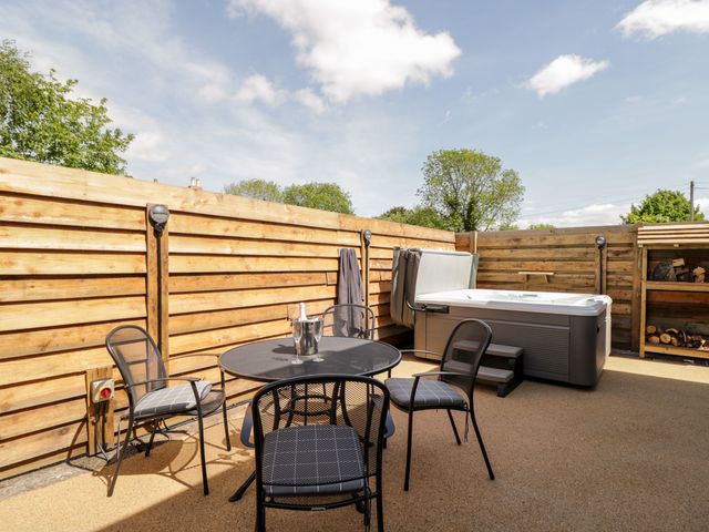 An outdoor patio area with a round metal table and four chairs a hot tub and a wood storage shelf at Little Lugg in Cross Keys near Hereford