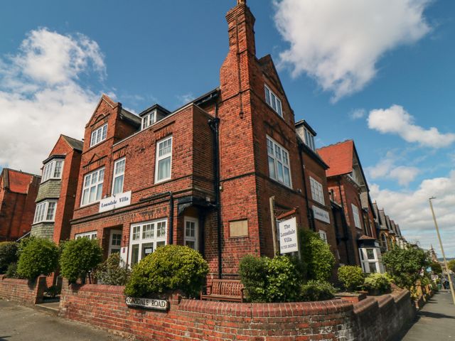 A red brick building with white window frames and greenery along the brick fence at Lonsdale Villa in Scarborough