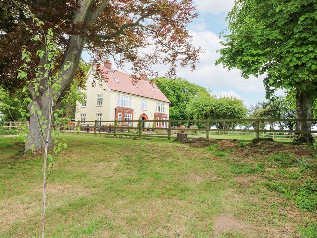 A two-story house with a red roof surrounded by trees and a wooden fence at High House in Southrepps