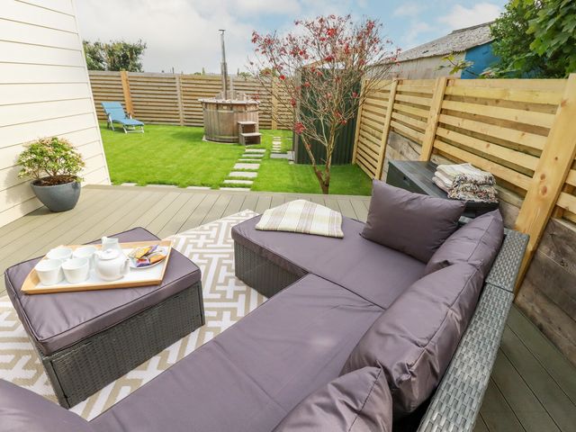 A garden patio with outdoor seating and a tea set on a table a hot tub on grass behind a wooden fence at Badgers Sett in Tintagel
