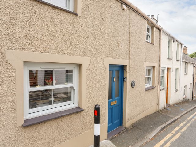 A street with a beige house with a blue door and a window with white frames at Osborne House in Menai Bridge