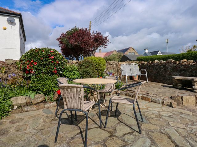 An outdoor patio with a round table and four chairs surrounded by plants and a stone wall at Angorfa Bach in Abersoch
