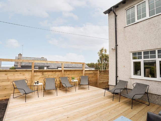 A wooden deck with six gray chairs and two small white tables outside a house with fenced yard at Hillcroft in Abersoch