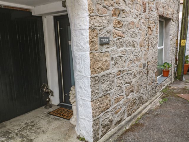 The exterior stone wall of a building with a dark door a welcome mat horse sculpture and potted plants at Troika in Newlyn