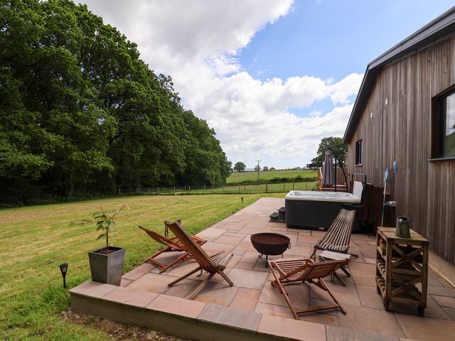 An outdoor patio with wooden chairs a hot tub a fire pit and a potted plant next to a wooden building at Quantock Barn in Stockland near Honiton