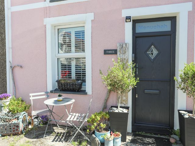 A small outdoor seating area with a table and two chairs next to a window and a dark door at Menuchah in Criccieth