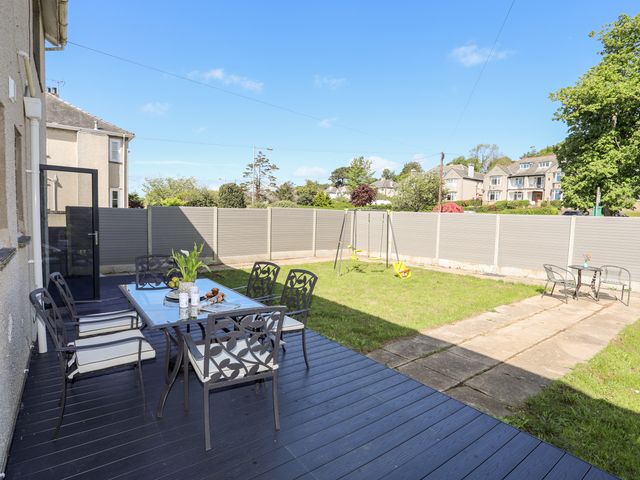 A backyard with outdoor dining table and chairs on a deck a swing set and a small table with chairs at Glan Aber in Pwllheli