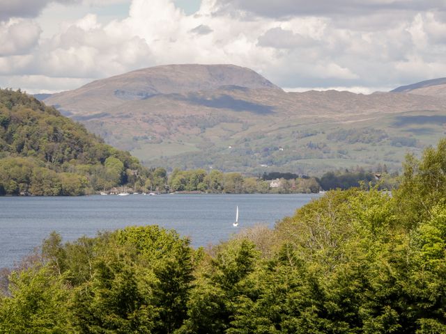 A lake with a sailboat surrounded by trees and hills at Howgill Lodge in Gatebeck near Kirkby Lonsdale