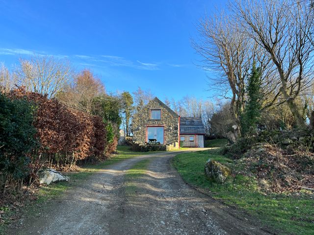 A stone house with a gravel driveway and trees at Pen y Mynydd in Newport Pembrokeshire