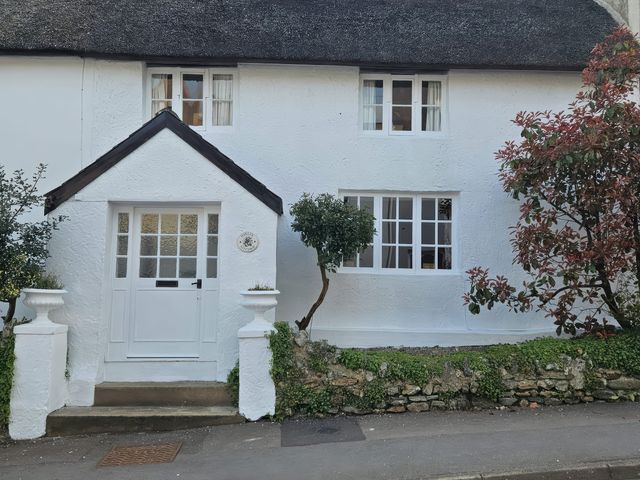 A cottage exterior with a thatched roof and front door at Foxley Cottage in Charmouth