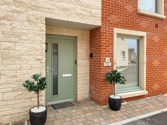 The front entrance of a house with a green door and a window beside it with plants in black pots on a paved area at Sea Gem in Castletown Portland