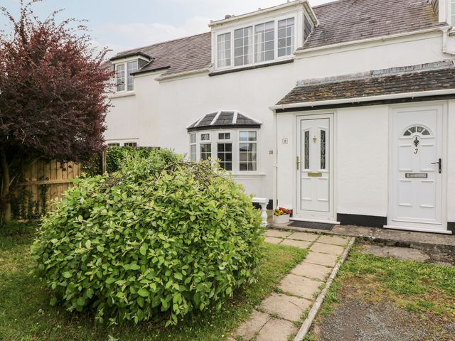 A front garden with a paved path leading to two white doors on a white house with windows and shrubs at Woodview Cottage Jeffreyston near Tenby