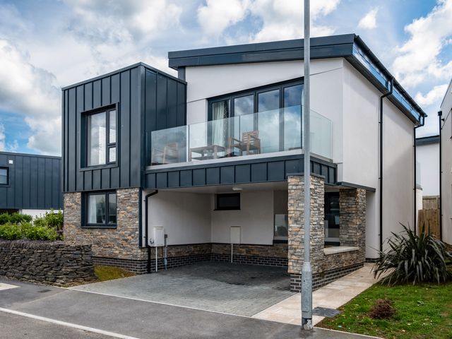 A modern house with a covered carport and glass balcony with chairs at Beach Haven in Perranporth