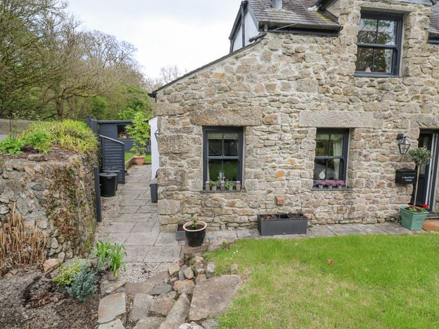 Stone cottage exterior with windows and potted plants on a grassy lawn at Wood Brook Cottage in Crowan