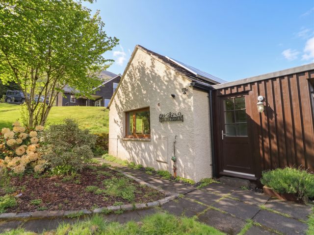 An exterior view of a house with a flower bed and pathway at Puidrac Cottage Balquhidder
