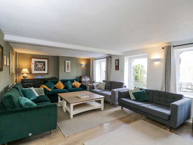 A living room with green and gray sofas a wooden coffee table and framed pictures on walls at The Old School House in Lower Swell near Stow-On-The-Wold