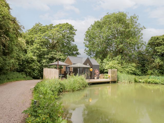 An outdoor area with a house by a pond at Maple Lodge at Bridge Lake Farm & Fishery Chacombe
