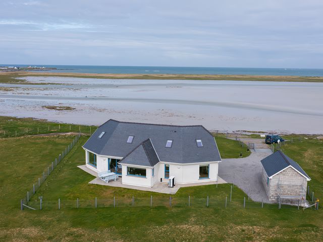 A house with a fenced yard near a beach and a small outbuilding at Gualan Sands in Iochdar