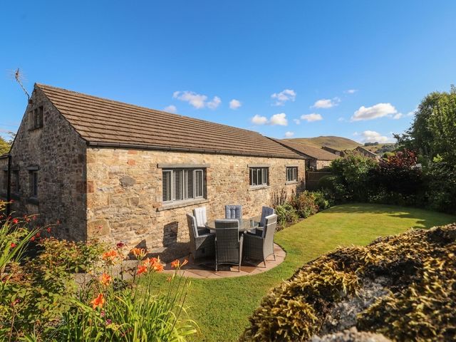 A stone cottage with a table and chairs in the garden at Glen Lea in Giggleswick, Settle