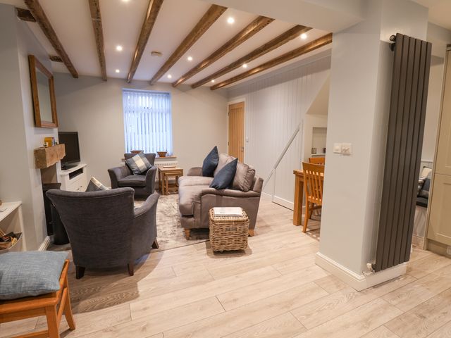 A living room with a sofa and armchairs a wooden dining table and chairs and exposed ceiling beams at Rockfish Cottage in Staithes