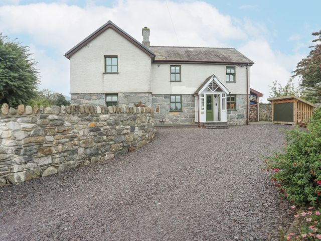 A gravel driveway in front of a two-story house with a stone wall and a wooden shed at Bronfa in Tregarth near Bethesda