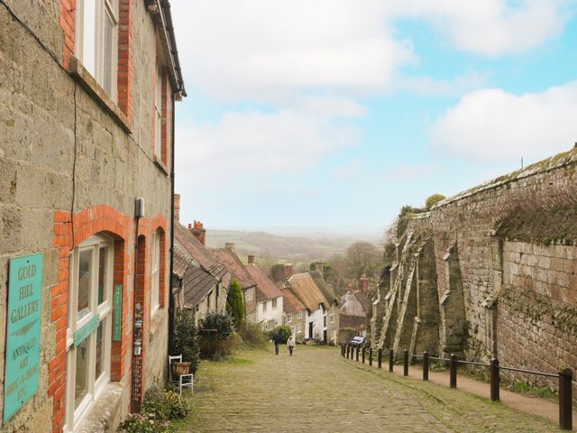 A cobblestone street descending between old stone and brick buildings and a large stone wall with countryside in the background
