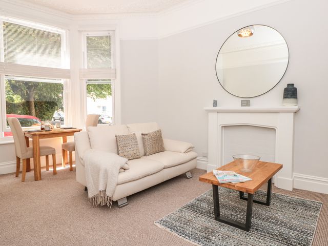 A living room with a white sofa coffee table by a fireplace and a dining table with chairs by the window at Flat 1 Byfield in Torquay